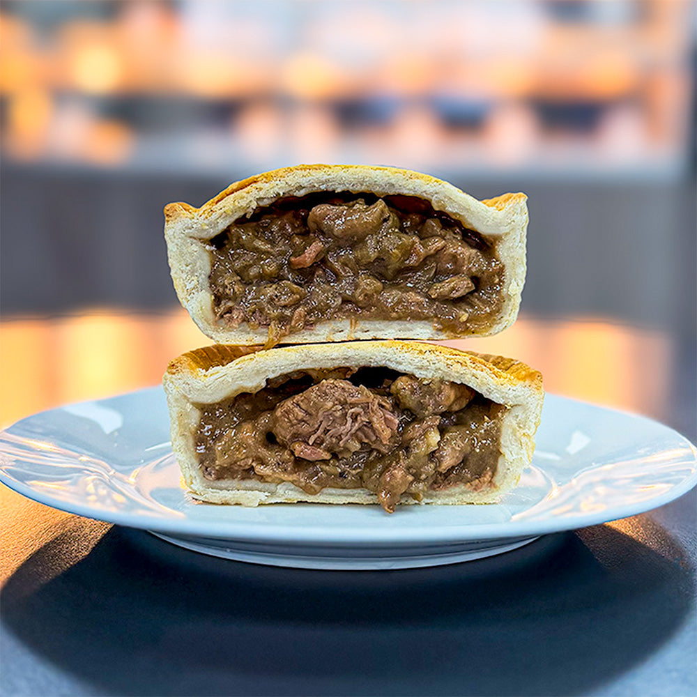 A peppered steak pie cut in half on a plate, ready for pie delivery across the UK.